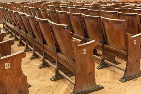 Antique wooden armchairs arranged in rows in a concert hall. Shabby surface, leather seats. Blurred image of chairs in the background.の写真素材