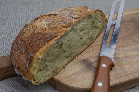Multigrain sliced bread on a wooden kitchen board. A kitchen bread knife is lying nearby. Pumpkin...