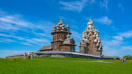 Landscape on the Kizhi island in Lake Onega on a summer sunny day. View of a green meadow with ancient architecture in the background framed by blurry tree branchesの写真素材
