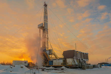 Drilling wells in the winter at an oil and gas field in the Arctic. Polar day with textured beautiful sky. Steam puffs for heating equipmentの写真素材
