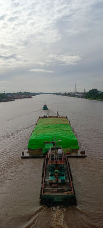 A barge is heavily loaded with cargo, and being pushed by a tugboat directly behind it.の写真素材