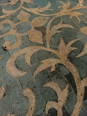 The courtyard floor decoration features swirling, organic, vine-like motifs made from small, textured, light-colored pebblesの写真素材