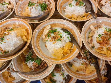 Several bowls of chicken soto, Indonesian dish, filled with white rice, topped with shredded chicken, glass noodles, fried shallots, fried potato slices and fresh green herbs likeの写真素材