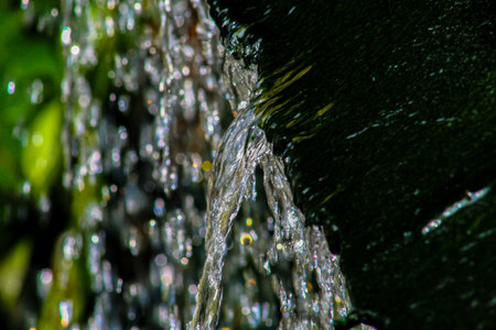 The beautiful movement of water as it flows from the dark, textured surface of a natural rock...