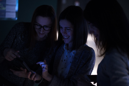 Horizontal indoors shot of women smiling and browsing smartphone at night. の写真素材