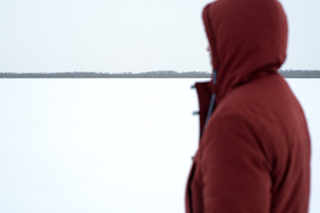 Side view of man in red warm coat posing on background of snowfield looking away. の写真素材