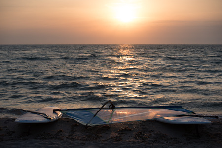 Landscape of sandy beach with windsurfing boards lying on background of sea in sunset light.の写真素材