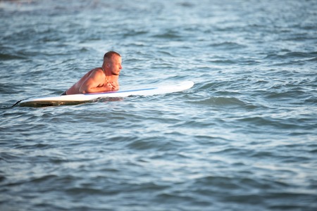A man with SUP waist-deep in the sea is looking forward to the sunsetの写真素材