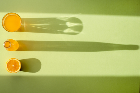Orange soda in a clear glass beaker, a bottle and a slice of orange on a green surface under Sunny lightの写真素材
