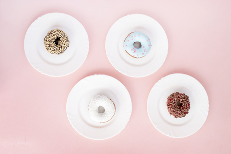 Four white plates with different donuts covered with glaze on pink backgroundの写真素材