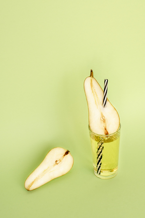 Light pear juice in a transparent glass beaker with a straw, striped, and half of pear on a green background. Still-life.の写真素材