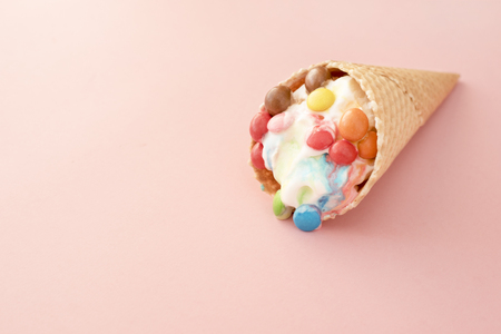 Ice cream in a waffle cone with colored candy toppings on a pink backgroundの写真素材