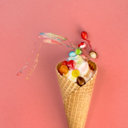 Ice cream in waffle cone with multicolored candies in filling smeared on pink background