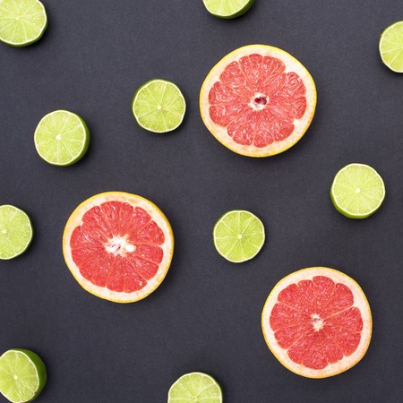 Background of red grapefruit and green lime split in half on black backgroundの写真素材