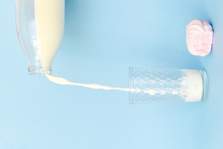 From a transparent glass bottle pour milk into a glass glass. Blue background. Pink bitten...