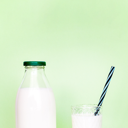 Milk in  glass bottle and transparent glass with straw on  green backgroundの写真素材