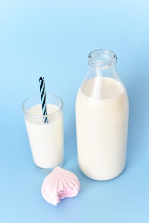 Milk in  glass bottle and in  glass and marshmallow on  blue backgroundの写真素材