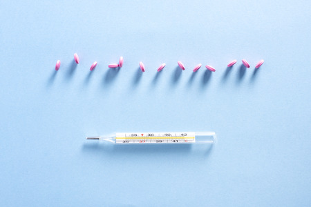 Thermometer and pink pills on blue background