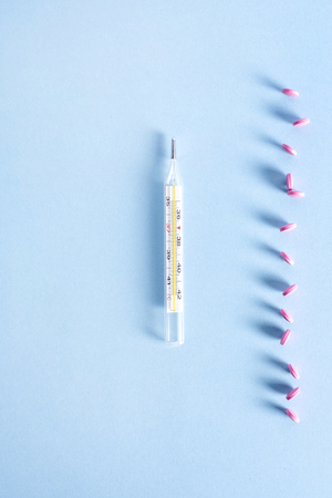 Thermometer and pink pills on blue background
