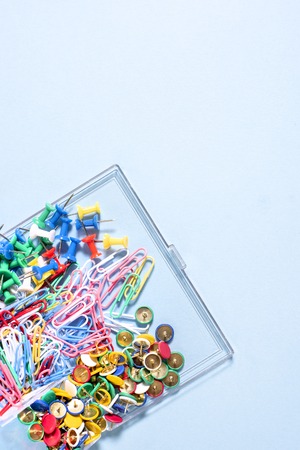 A set of stationery made of multi-colored buttons and paper clips in a box on a blue surfaceの写真素材