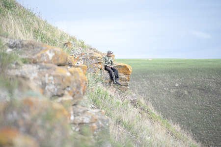 A man in uniform sitting on a rock on the side of the mountainの写真素材