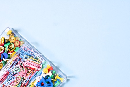 A set of stationery made of multi-colored buttons and paper clips in a box on a blue surface