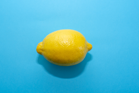 One whole ripe yellow lemon on a blue background with a shadow on the surfaceの写真素材