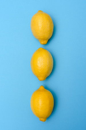 Three yellow lemons in a row on a blue surface. The view from the top.の写真素材