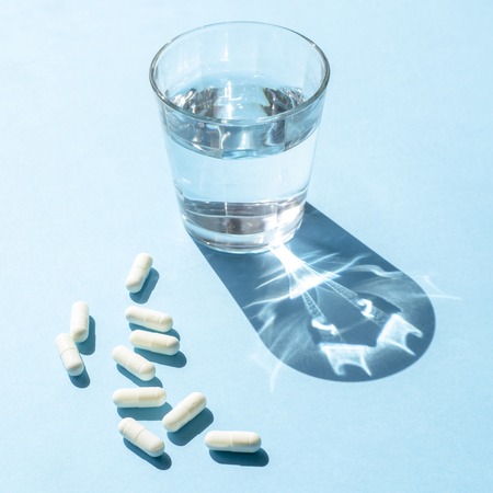 Water in a clear glass Cup and white long capsules on a blue surfaceの写真素材
