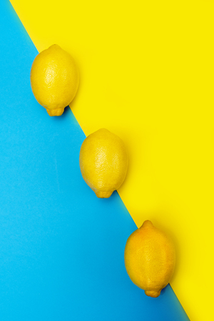 Three yellow lemons in a row on a yellow-blue backgroundの写真素材