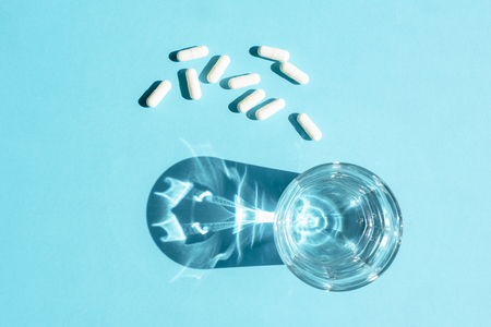 Water in a clear glass Cup and white long capsules on a blue surfaceの写真素材