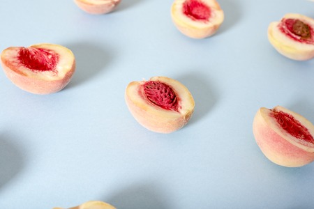 Ripe beautiful peaches with bones divided in half stacked in a row on a blue background.の写真素材