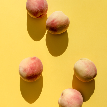 Whole ripe beautiful peaches on yellow background under natural lightの写真素材