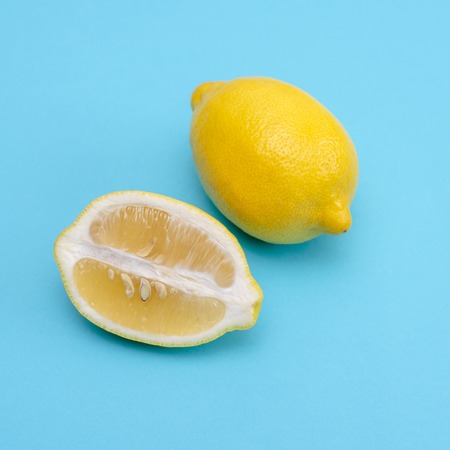 One whole ripe yellow lemon and cut along a piece on a blue backgroundの写真素材