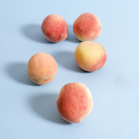 Whole ripe beautiful peaches on blue background with shadowsの写真素材