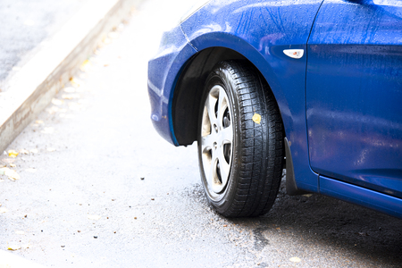 Car wheel on which one yellow leaf tree and the front of the blue car after the rainの写真素材