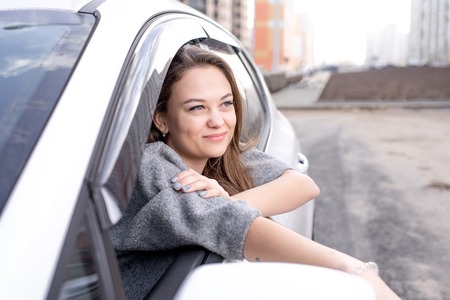 Beautiful caucasian girl sitting in a white car and looks out the windowの写真素材
