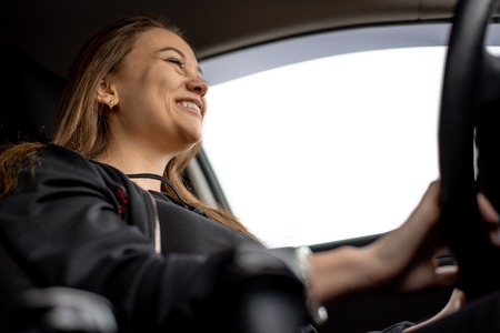 Beautiful young woman smiling in black clothes in car drivingの写真素材
