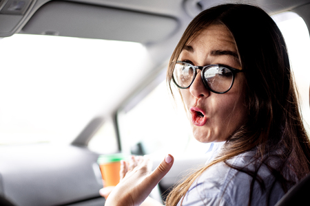 Girl with glasses expresses surprise sitting in the car on the passenger seatの写真素材