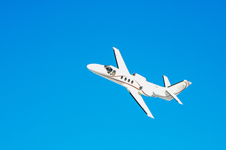 A small white private plane flies in blue skyの写真素材