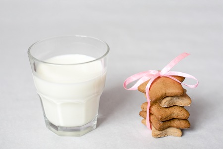 Christmas gingerbread in the form of stars tied with a pink ribbon and a glass of milk on white tableの写真素材