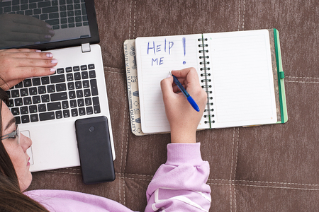 The woman was tired of working on a laptop on the couch and writing on a notebook "Help me"の写真素材