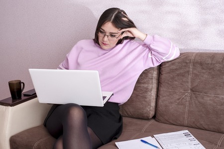 Student at home preparing to study sitting on the couch and studying the material on the laptopの写真素材