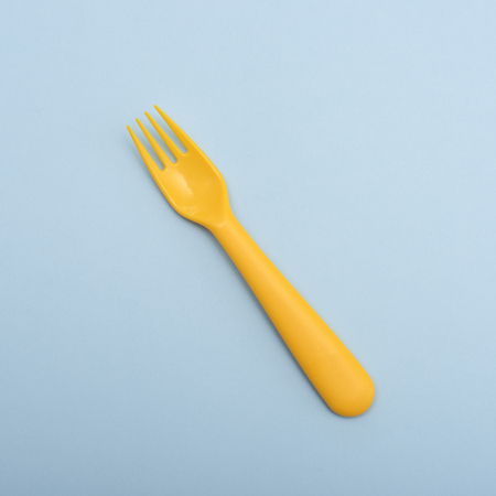 Yellow plastic fork on blue background . Minimalism.