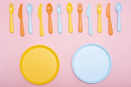 Colorful tableware : spoon, knife, fork and two plate yellow and blue color on pink background. Copy...