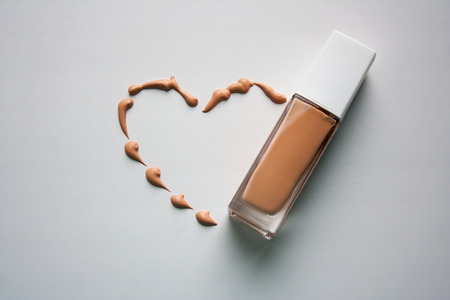 Beige dashed heart with face tonal cream bottle composition isolated on white backgroundの写真素材