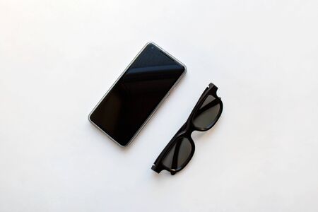 Modern mobile phone and black glasses isolated on white background from a high angle viewの写真素材