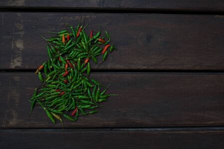 Heap of small green and red chili peppers isolated on dark wooden background from a high angle viewの写真素材