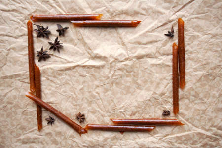 Rolled fruit pastila sticks and star anise spices frame composition on beige paper background