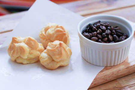 Eclair pastry with white paper Placed on a wooden tray.Eclairs on white paper and coffee beans in...